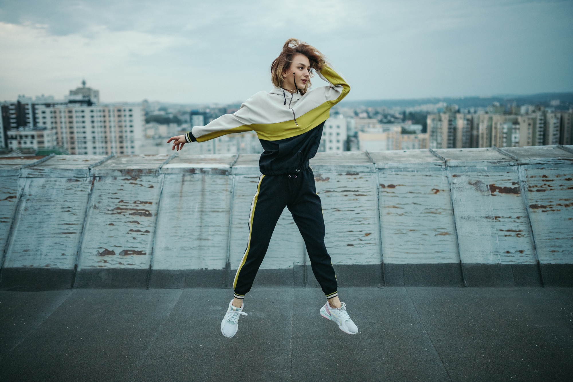 Trendy woman in sportswear jumping on rooftop